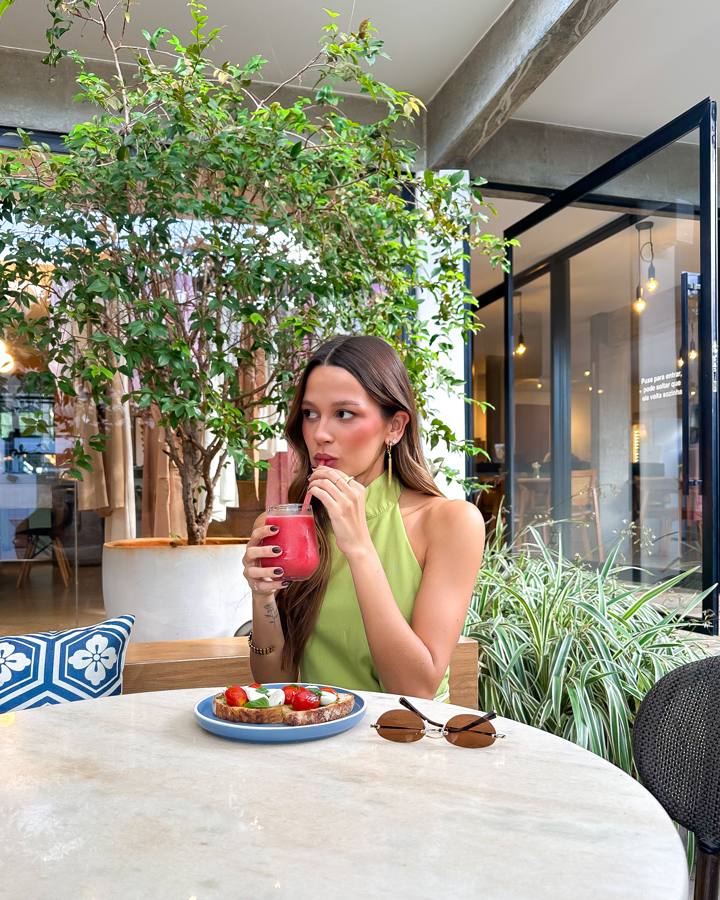Cliente tomando suco na área externa, com bruschetta de tomate e muçarela na mesa de mármore