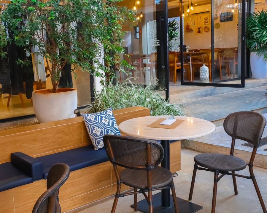 Mesa de mármore na área externa, com almofada azul e plantas ao fundo