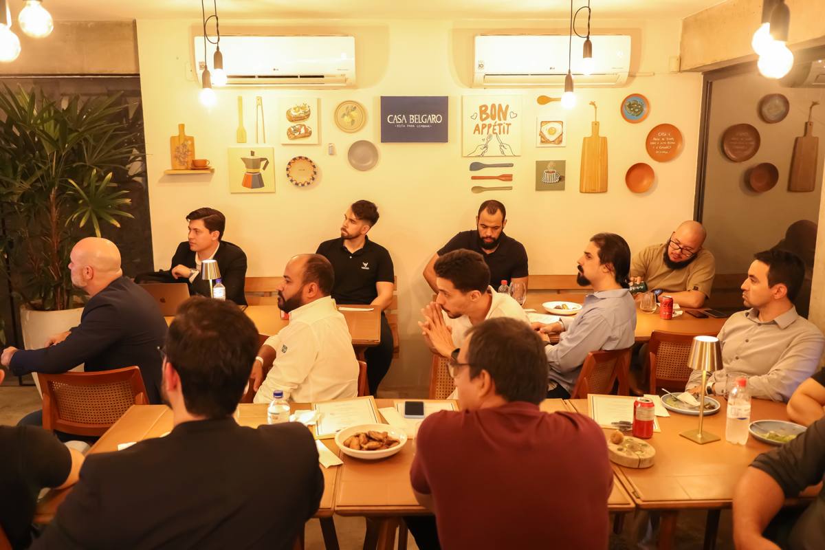 Confraternização de empresa no salão interno, com mesas unidas e convidados atentos à fala do anfitrião