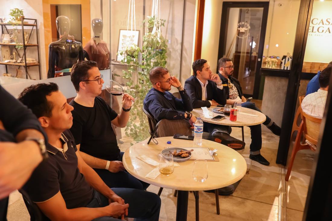 Amigos em mesas redondas de mármore, com taças de vinho e petiscos